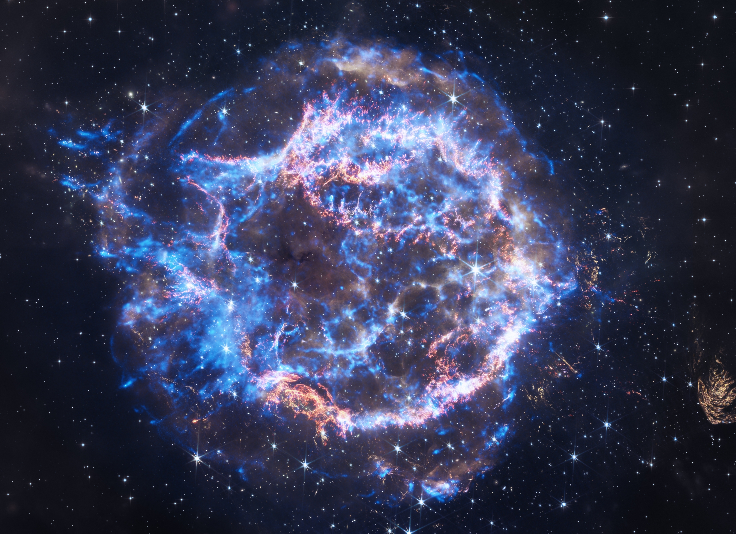 Here, rings of neon blue and brilliant white emit veins of polished gold. The rings and their arching veins encircle a place of relative calm at the center of the supernova remnant. This hole at the center of the circle, and the three-dimensionality conveyed by the rings and their arching veins, give this image of Cassiopeia A the look of a giant, crackling, electric blue donut. 