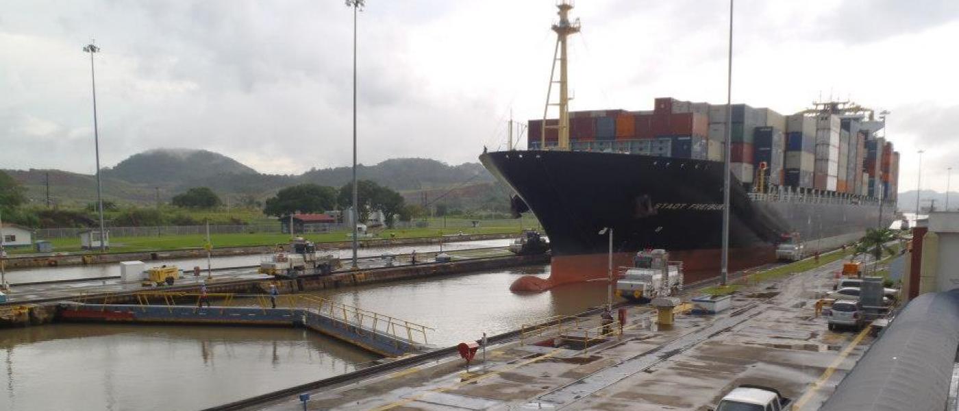 A large ship holding shipping containers moves through the Panama Canal.