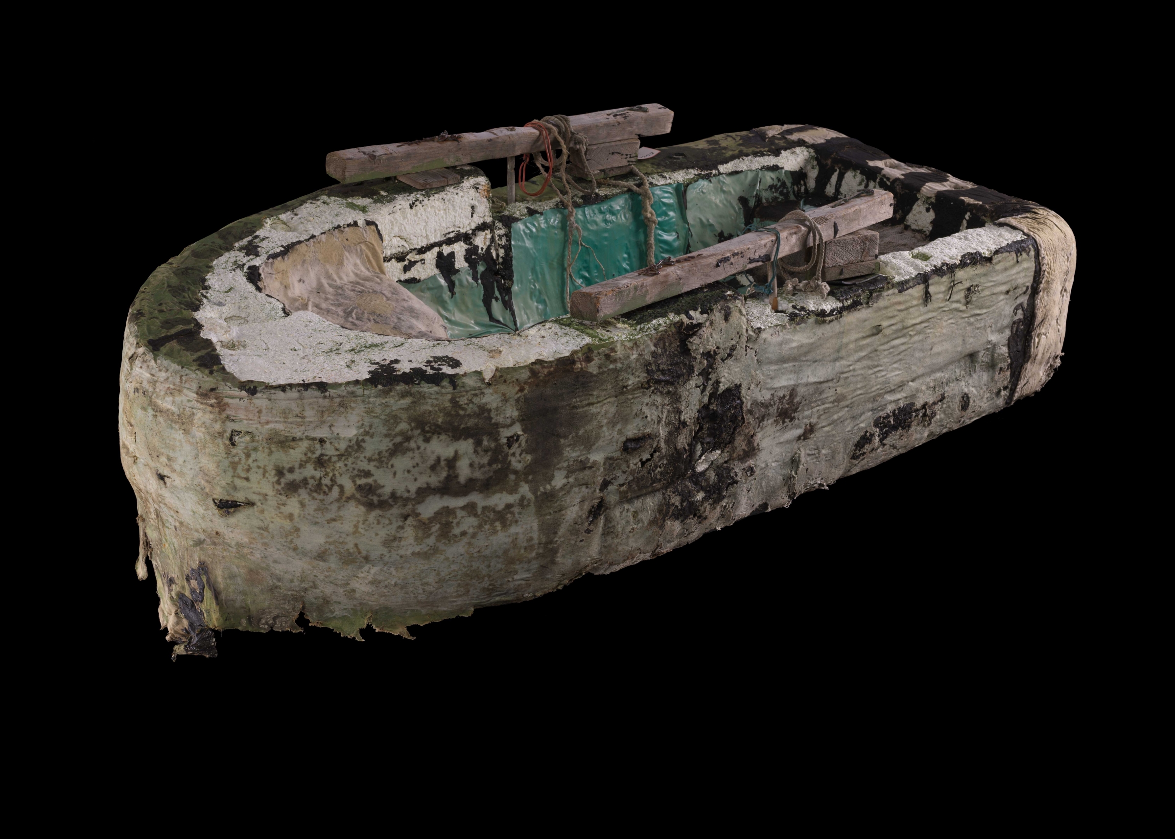 Handmade raft with a body of foam and wood. There is tar and cloth coating the exterior and blue, plastic sheeting covering interior parts