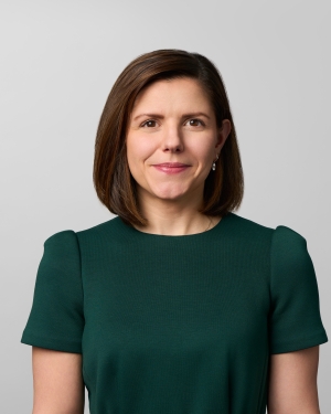 Woman with brown shoulder-length hair and a green short sleeve dress smiles toward camera.