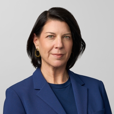 Woman with brunette bob in a deep blue suit smiles toward camera.