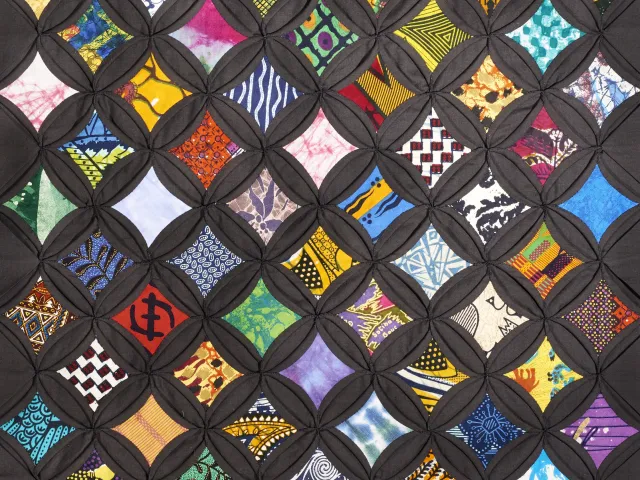 Brightly colored African batik and printed fabrics are set within a matrix of black cloth, rendering vividly the effect of a stained-glass window. 