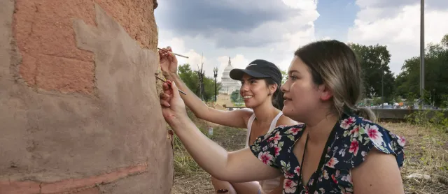 Two interns assess a stone wall with the Capitol building in the background.