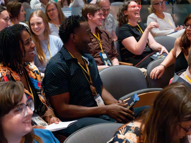 A group of people sitting in rows of chairs smile and converse with each other. 