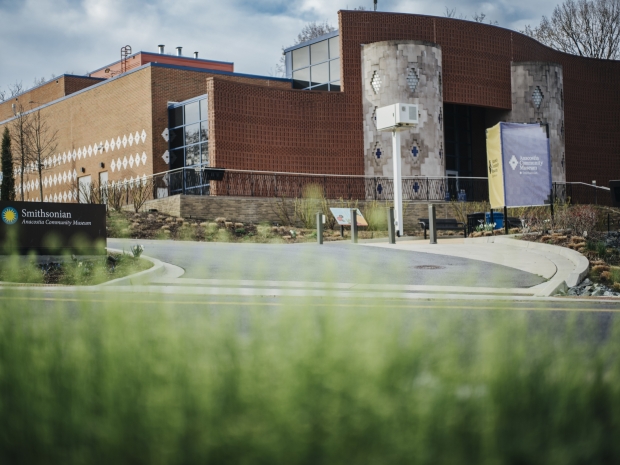Exterior of a building with red brick and iron design features, with a curved road leading up to it. 