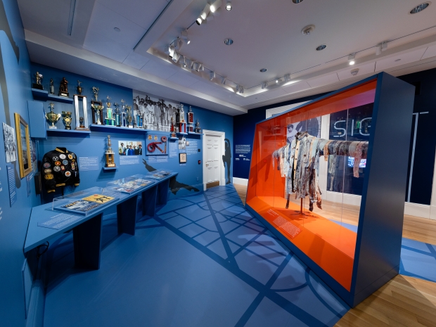 Gallery view of exhibition with blue walls and floors and a glass case with a jacket inside. 