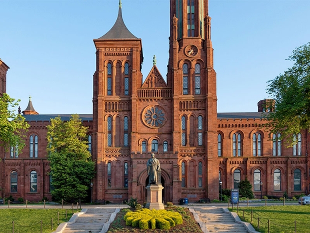 Smithsonian Castle and sunburst topiary in front of statue 