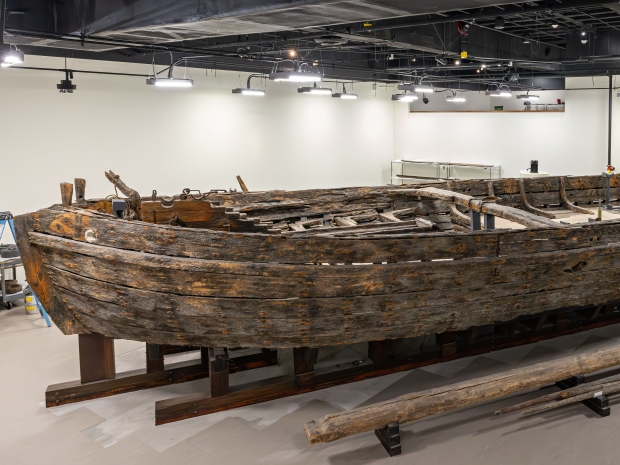 Large wooden boat sits in well-lit conservation space.