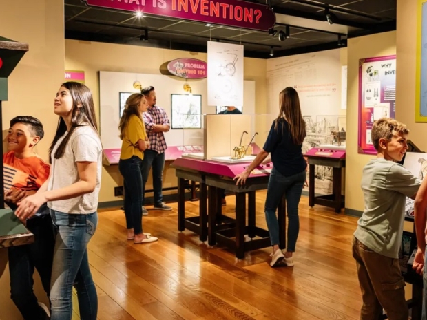 Seven people- adults and children- interact with the Nation of Inventors exhibition gallery