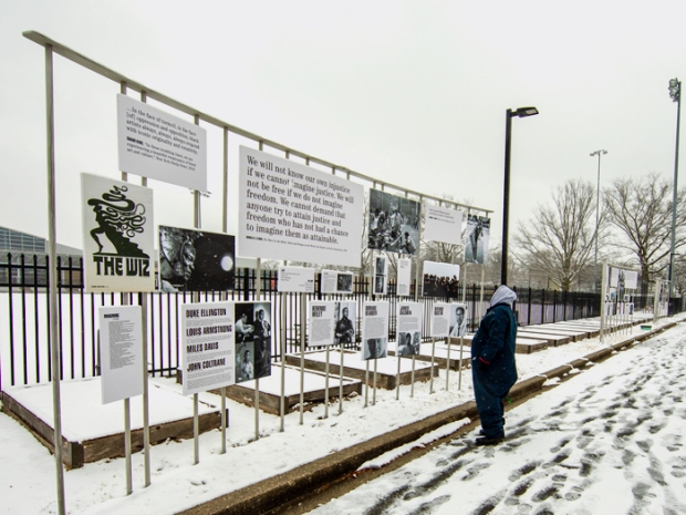 Person stands in snow looking up at art attached to a fence