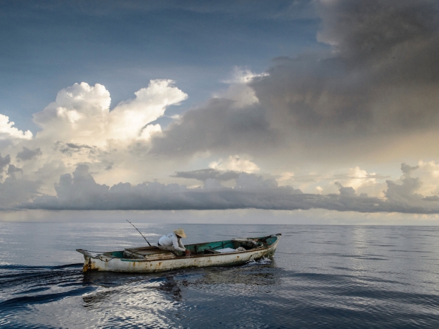 Lone fisherman in small boat against dramatic sky
