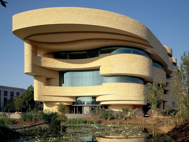 Exterior of light, natural stone building with undulating sides and curved windows. 