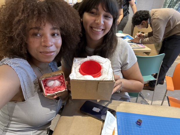 Two young people smile at camera and hold up objects. 