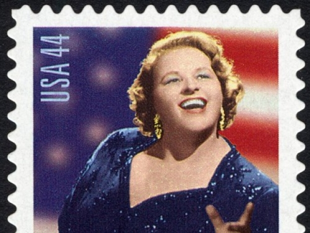 USA stamp with woman singing in front of a flag