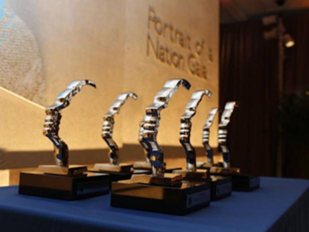 A group of awards with silver hand sculpture and wood base sit on a podium. 