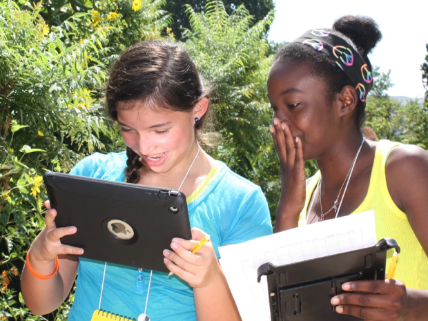 Two girls look at data on a digital device in the field.  