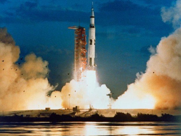 Apollo 4 launches into a dark blue sky amid smoke on the ground.
