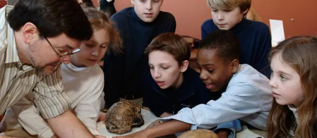Anthropologist with group of young students examining artifacts