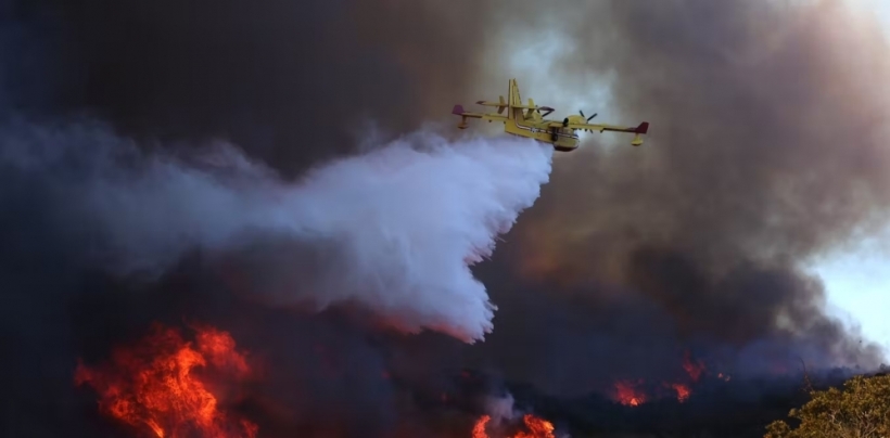 A plane dumps water onto a burning hillside