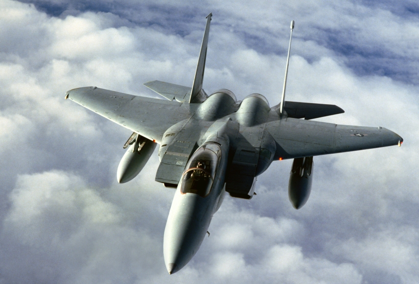 A fighter plane with narrow nose and wide wings in a light gray color flies above the clouds.