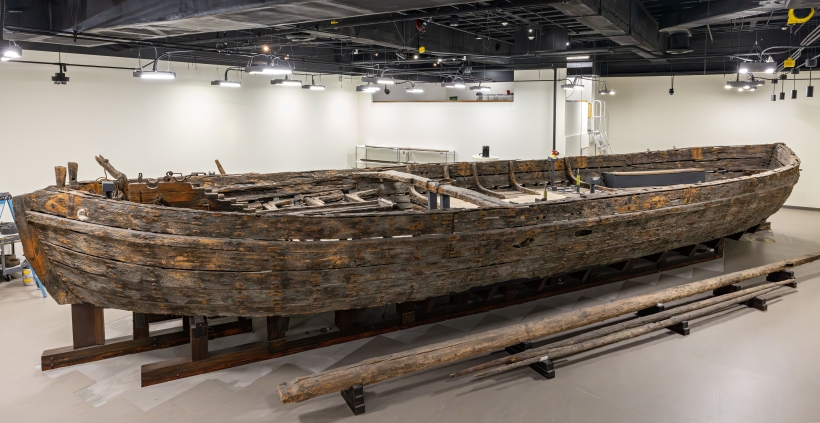 Large wooden boat sits in well-lit conservation space.