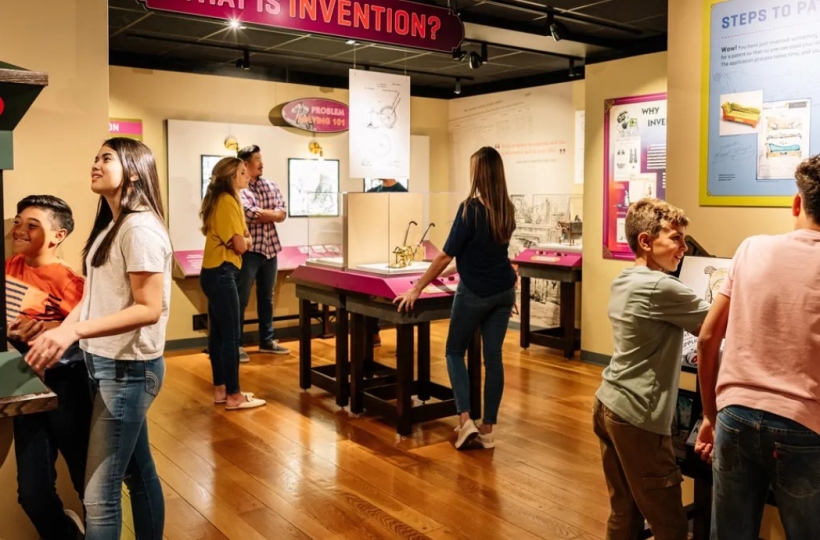 Seven people- adults and children- interact with the Nation of Inventors exhibition gallery