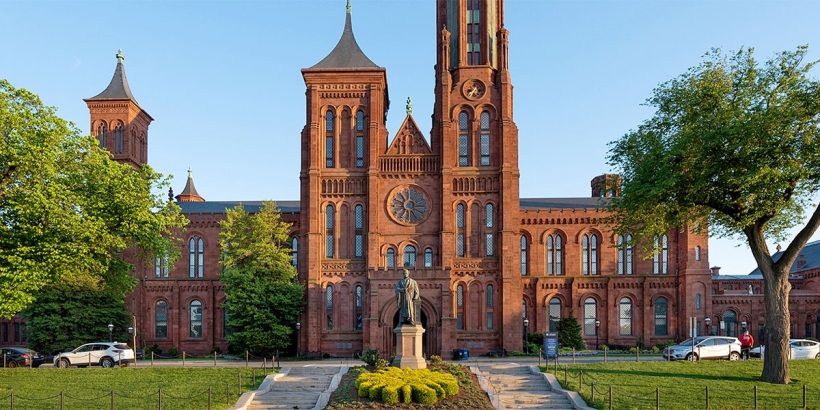 Red brick building with large windows, spires and manicured landscaping in front.