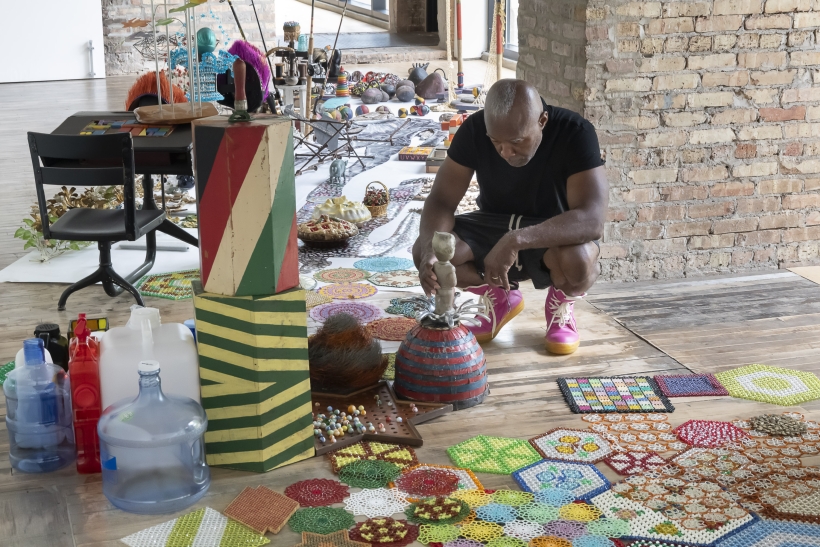 A man crouches down by vibrant painted and patterned art objects.