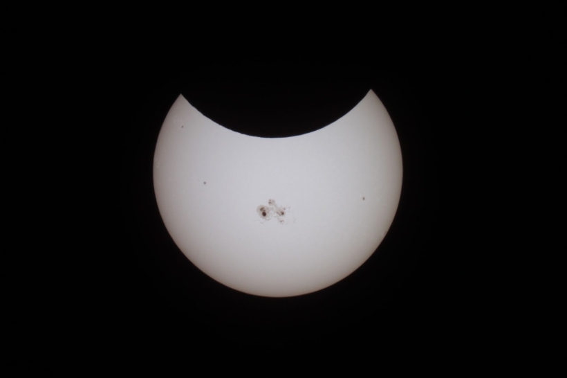 Photo of the sun in black white, with a partial eclipse creating a half-circle black shadow on top part of sun. 